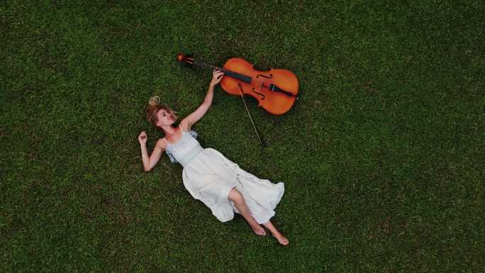 躺在绿草地上拉大提琴的美女