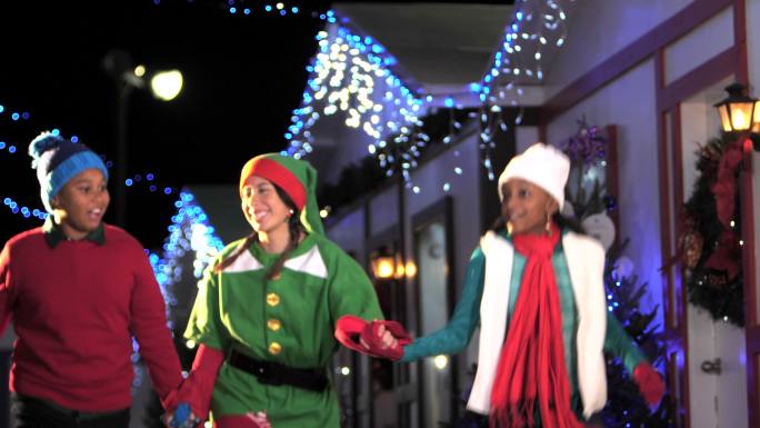 圣诞老人的小精灵带着两个孩子在村子里蹦蹦跳跳