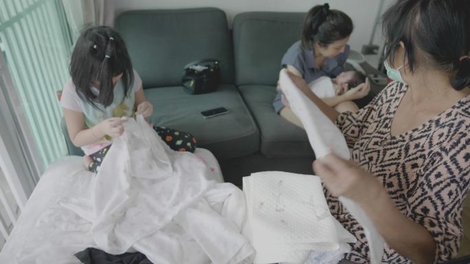 奶奶和孙女把哥哥的尿布和衣服叠在沙发上。