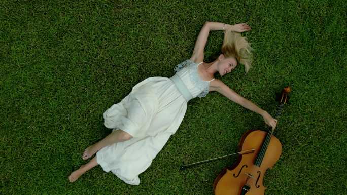 躺在绿草地上拉大提琴的美女