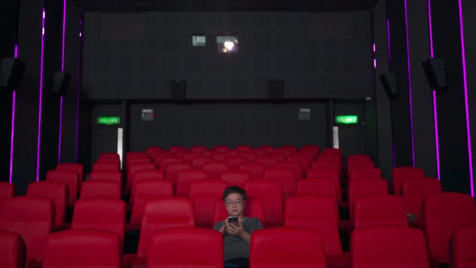 亚裔中国中年女性独自在电影院看电影时查看智能手机信息，表情茫然