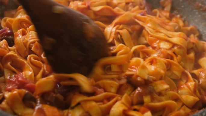 慢动作搅拌和烹饪tagliatelle意大利面，配番茄酱、橄榄和蘑菇