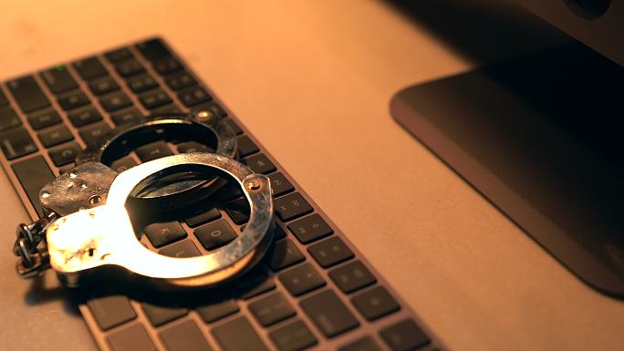 网络犯罪概念。金属手铐放在电脑键盘上的平移镜头。
