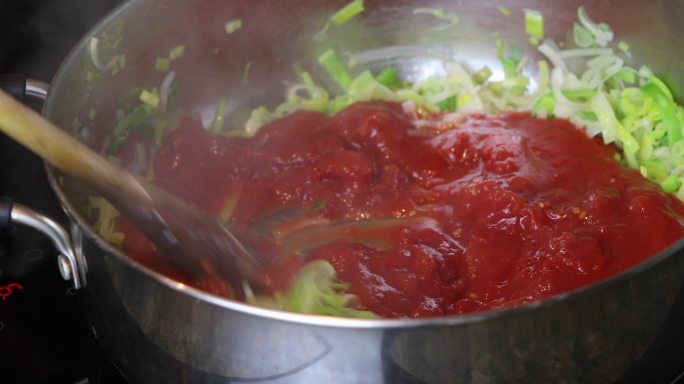 将切好的西红柿倒在大煎锅里炸韭菜上，然后用木勺搅拌