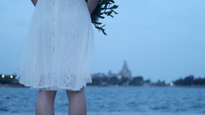 海堤旁少女穿着白色裙子手拿鲜花