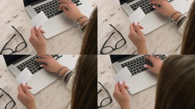 一名年轻女子在手提电脑上打字，同时用手中的名片寻找业务