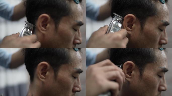 特写镜头中，亚裔中国男性美发师在酒吧里用经典剃须刀剃男人的头发。理发店。