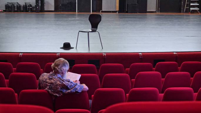 导演在一个空荡荡的剧院里写剧本，那里有红色的椅子和空荡荡的舞台