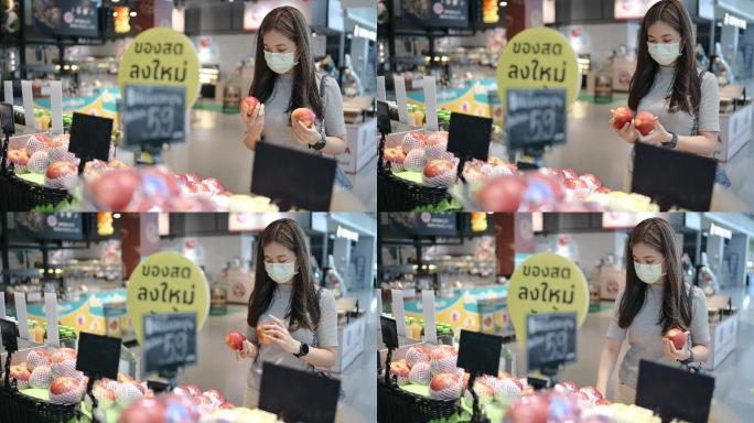 社交距离概念亚洲女性戴着防护面罩，晚上在超市选择西红柿、蔬菜和水果