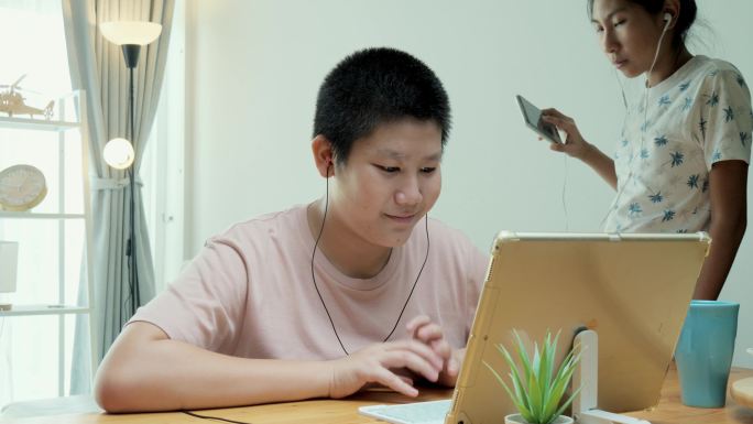 在2019冠状病毒疾病期间，一名亚洲女孩打断了她的弟弟，当时他正在家里餐桌上用数字平板电脑学习在线课