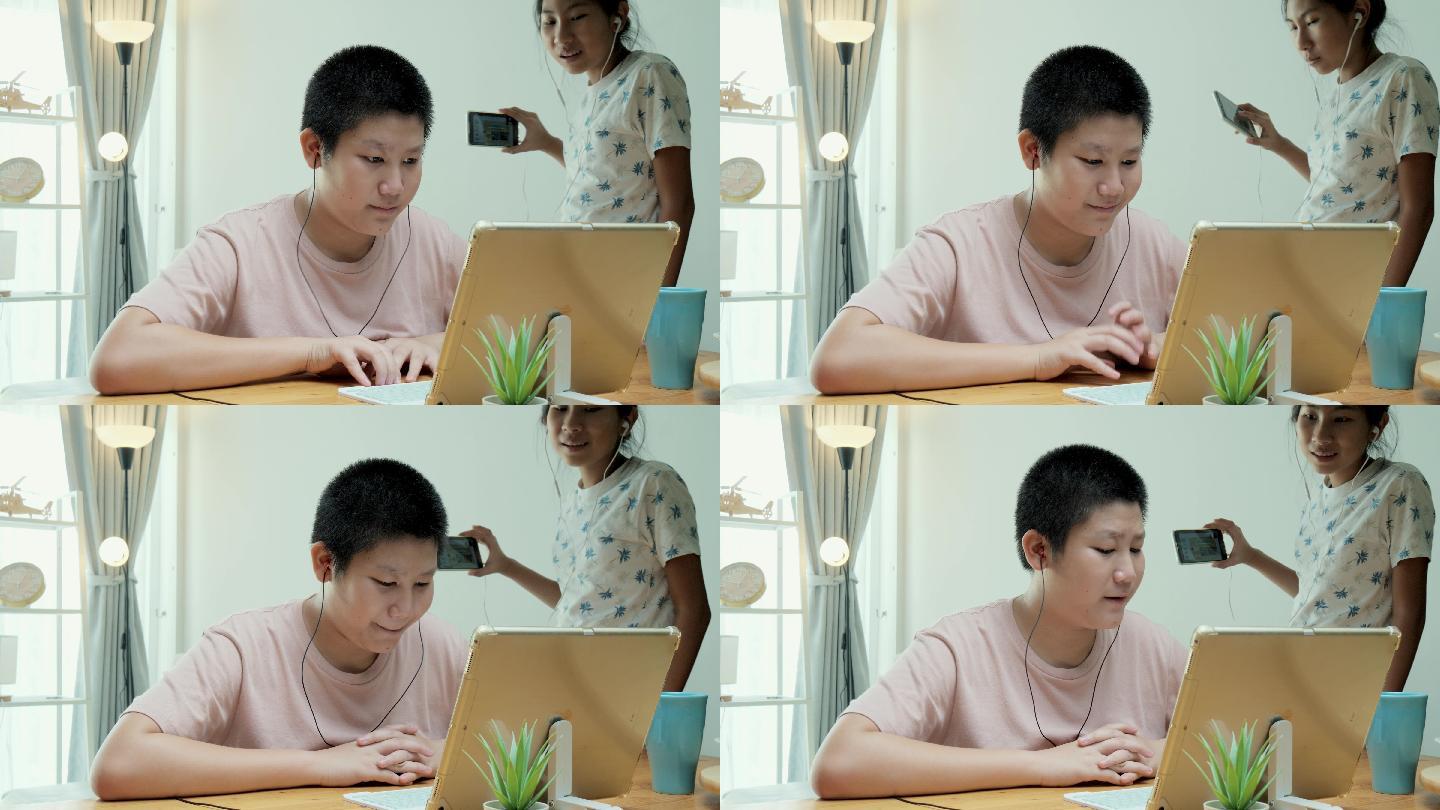 在2019冠状病毒疾病期间，一名亚洲女孩打断了她的弟弟，当时他正在家里餐桌上用数字平板电脑学习在线课