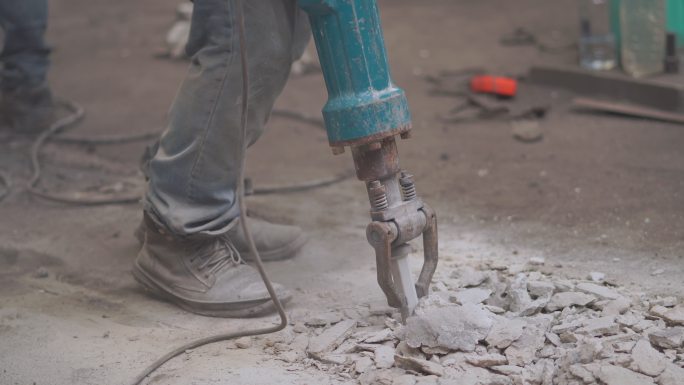 工人用手锤凿掉混凝土地板，钻混凝土地板进行维修，努力拆除工厂的建筑