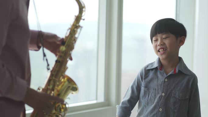 亚裔中国儿子在周末休闲时间欣赏和欣赏父亲演奏萨克斯管