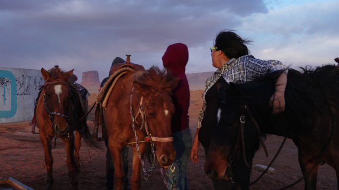 傍晚，在壮观的天空下，纪念碑谷的两个纳瓦霍小姐妹在照料马匹