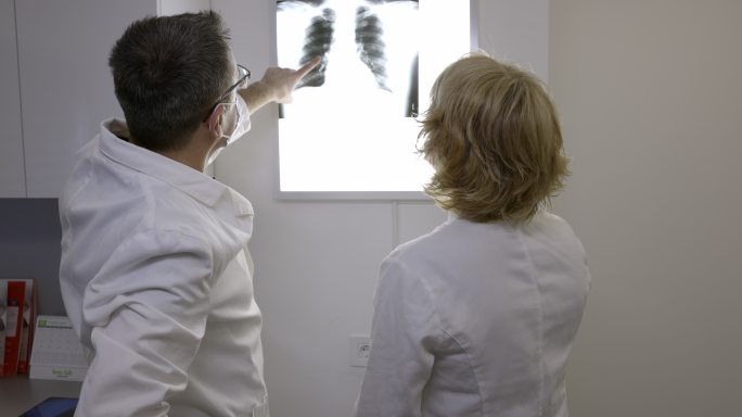 放射科医生戴着防护面罩在negatoscope上看X光的后视图