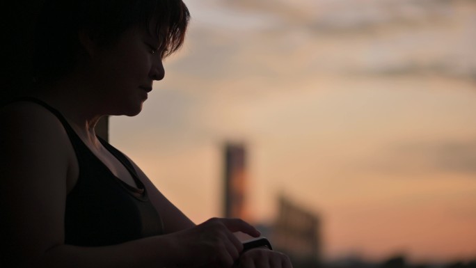 在剪影中，亚洲中国人身体呈阳性的中年女性早上在家锻炼后，用健身跟踪器检查心跳