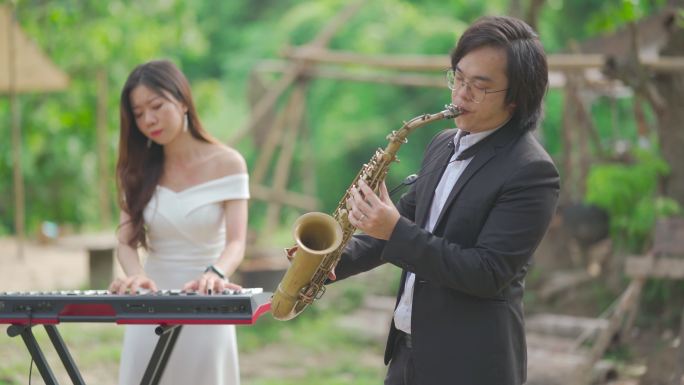 亚裔中国夫妇萨克斯管键盘演奏乐队穿着正式服装在农村进行练习