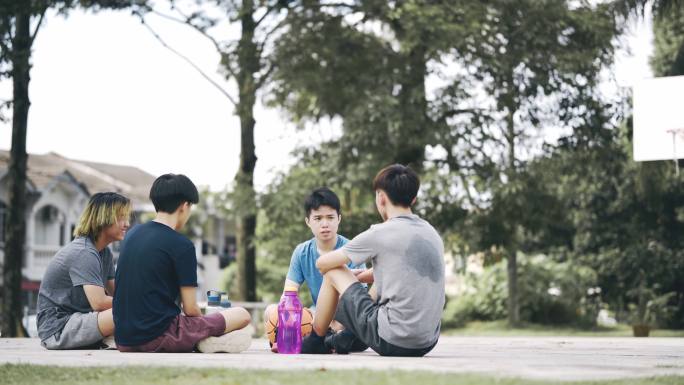 亚裔中国少年篮球运动员赛后与朋友坐在地上休息时喝水