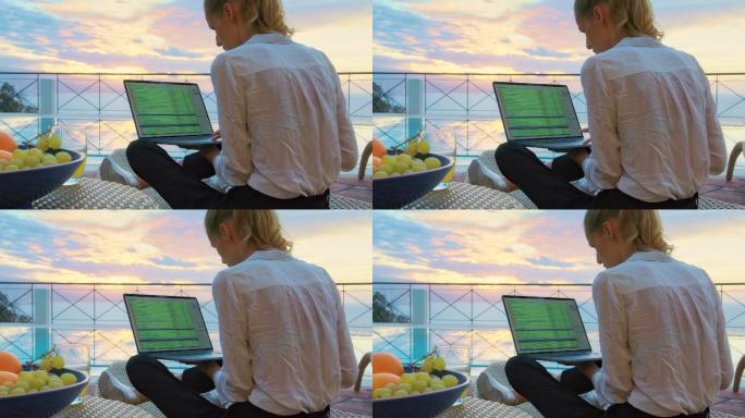 在院子里工作的女人。使用笔记本电脑欣赏史诗般的海景