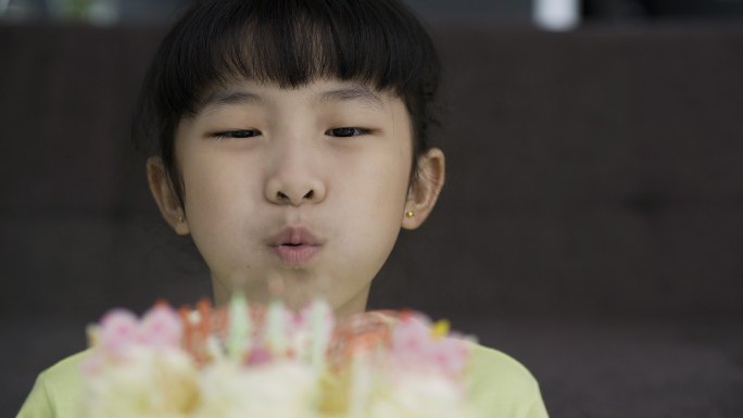 一个快乐的小女孩吹灭生日蛋糕上蜡烛的特写镜头。