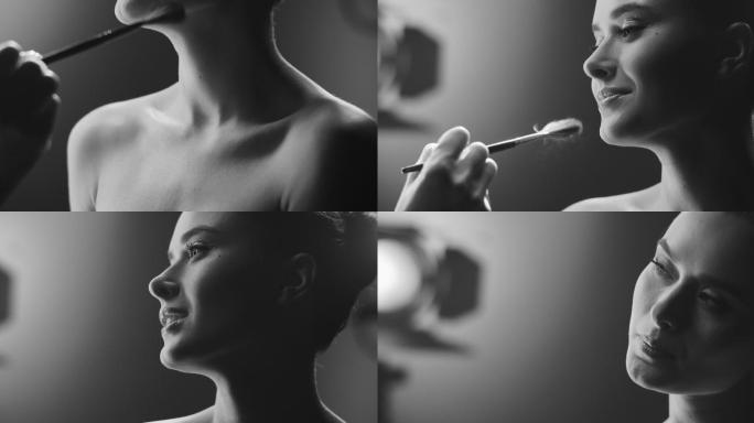 化妆师在片场用化妆刷将荧光笔涂在裸体女演员的脸上。黑白视频。