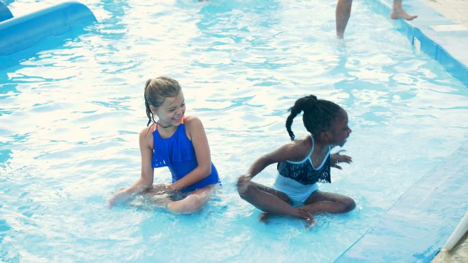 两个女孩坐在游泳池里互相泼水