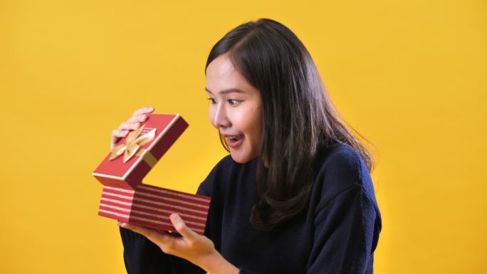 亚洲女性在工作室黄色背景上打开盒子