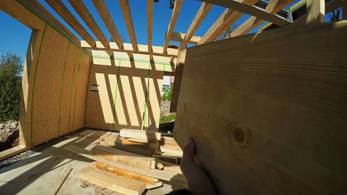 POV建筑商穿过正在建造的预制房屋的第一层，并携带木梁