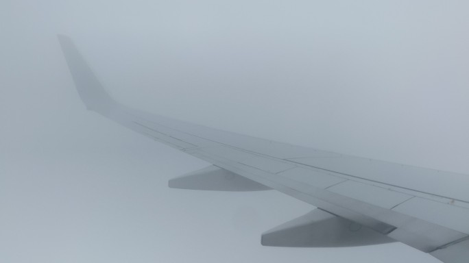 从一架商用飞机的机翼上俯瞰，这架飞机在晴朗的天气里飞越云层降落