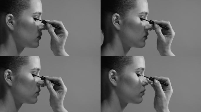 一位化妆师在模特的眼睛上画了一个带眼线笔的箭头，模特的特写侧视图。黑白视频。