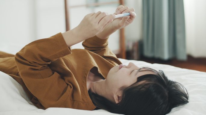 躺在床上拿着阳性妊娠检测试剂盒的亚洲女性