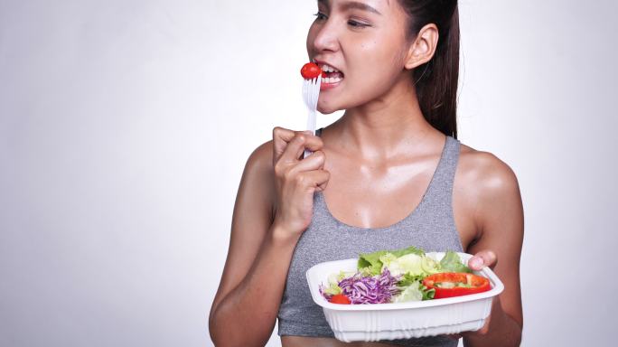 一位白人背景的年轻亚洲女性，为了美味的饮食，她吃沙拉、水果和蔬菜。