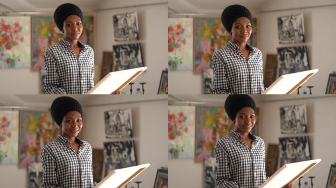 4K视频中，年轻的非裔美国女艺术家独自站在艺术工作室里，手持艺术画布看着相机