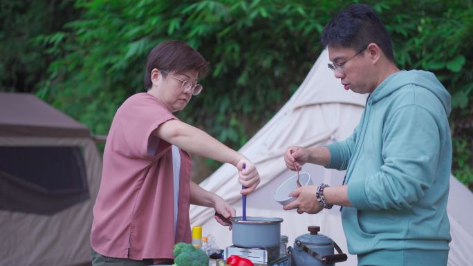 周末早上露营时，亚裔中国中年夫妇在帐篷旁准备早餐
