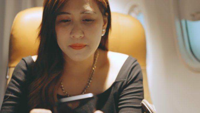 一名女游客坐在座位上，在飞行中使用手机。
