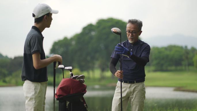 亚裔中国父亲在高尔夫球场教儿子打高尔夫球