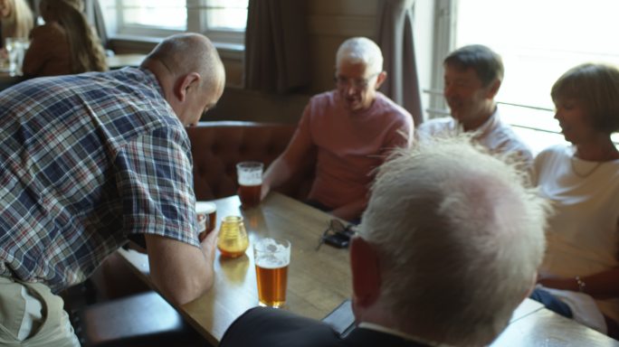 在拥挤的酒吧里，一名男子拿着啤酒走到桌子后的跟踪镜头