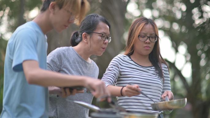 亚洲华人兄弟姐妹早上在露营时为家人准备早餐