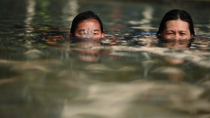 亚裔中国教练鼓励和教她的成年学生在游泳池中进行呼吸练习