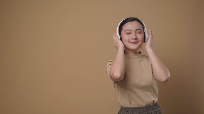 一位戴着耳机、独自站在背景上听音乐的快乐亚洲女性的肖像。