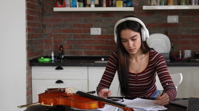 一位年轻而有才华的音乐学校女生在在线小提琴课上使用耳机。