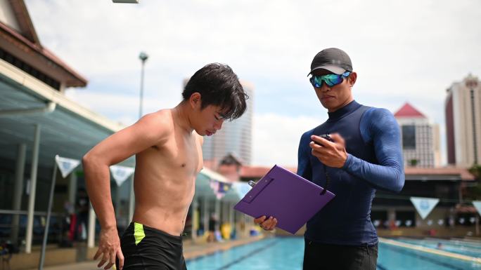 不高兴的亚裔中国私人教练在教育培训班结束后，在游泳池边展示了他的学生秒表