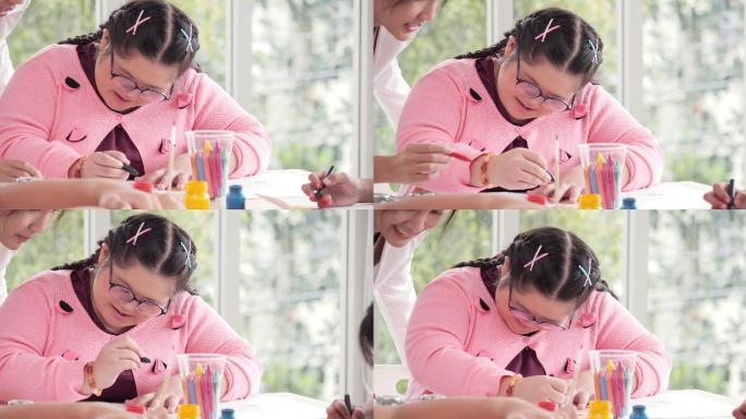 一个患有唐氏综合症的女孩坐在蜡笔旁画画，促进智力发展，一个女孩面带微笑，一位老师站在她旁边。