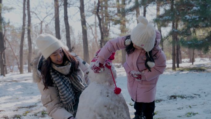 年轻妈妈和女儿在雪地里堆雪人