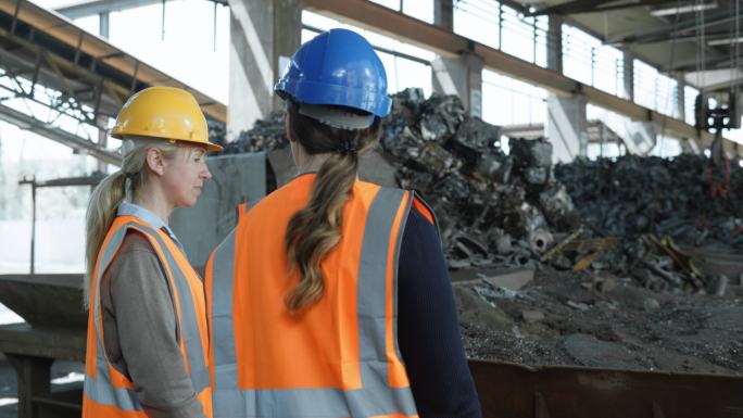 女性主管和女性运营总监走过回收设施的金属粉碎机