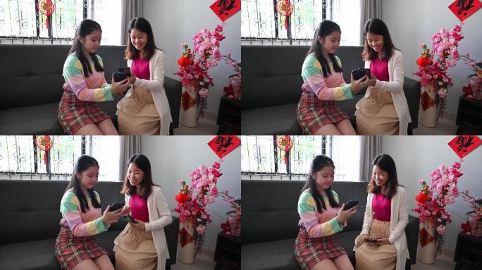 快乐的亚洲少女自豪地通过智能手机向母亲展示电子红包（数字Ang Pow）。
