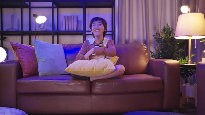在家里客厅的沙发上选择电视节目，在沙发上使用遥控器观看电视节目
