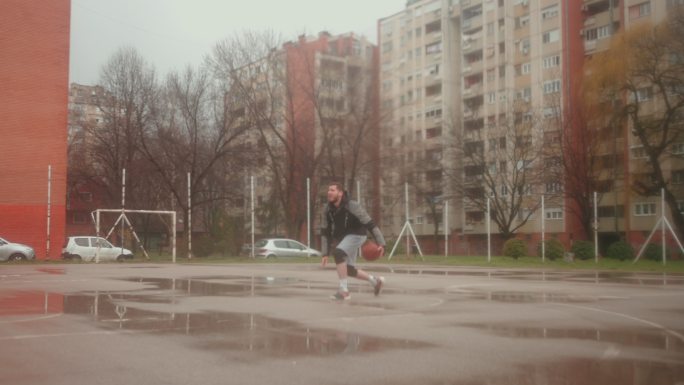 一名男子篮球运动员，在雨天的户外练习中长时间运球得分