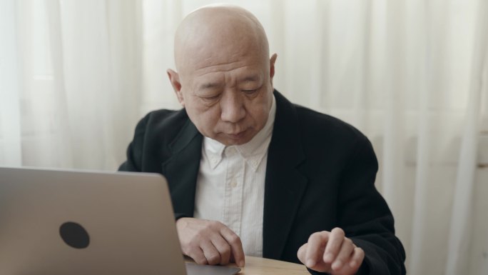 亚裔华裔无发老人使用笔记本电脑打字在开放式办公室工作