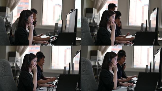 年轻的亚洲呼叫中心接线员戴着耳机在电脑上工作